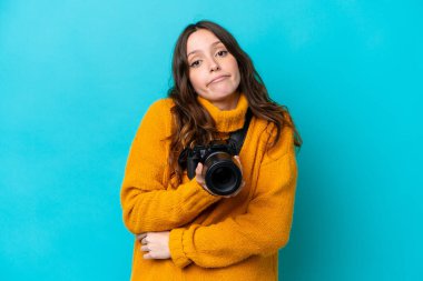 Mavi arka planda izole edilmiş genç fotoğrafçı kadın omuzlarını kaldırırken şüphe jestleri yapıyor.