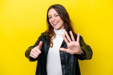 Sarı arka planda izole edilmiş genç beyaz kadın parmaklarıyla altısını sayıyor.