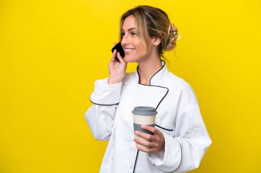 Uruguayan chef woman isolated on yellow background holding coffee to take away and a mobile