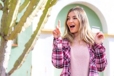 Genç, güzel Romen bir kadın, elinde kredi kartı tutarak çözümü bulmak için parmağını kaldırıyor.