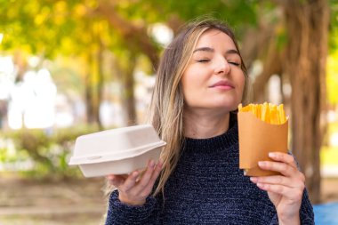 Genç ve güzel Romen kadın açık havada hamburger ve patates kızartması tutuyor
