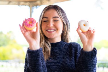 Genç ve güzel Romen kadın açık havada donut tutuyor.