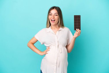 Genç Romen kadın mavi arka planda izole edilmiş hamile ve elinde çikolata tutuyor