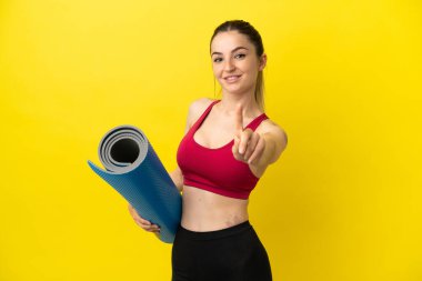 Young sport woman going to yoga classes while holding a mat showing and lifting a finger