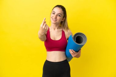 Young sport woman going to yoga classes while holding a mat doing coming gesture