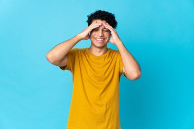 Genç Venezuelalı adam mavi arka planda izole edilmiş gülüyor.