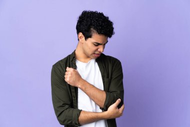 Genç Venezuelalı adam, mor arka planda izole edilmiş, dirseğinde ağrı var.