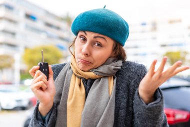Esmer kadın dışarıda arabanın anahtarlarını tutuyor. Omuzlarını kaldırırken şüpheli hareketler yapıyor.