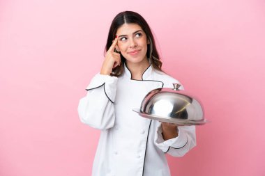 Young Italian chef woman holding tray with lid isolated on pink background having doubts and thinking