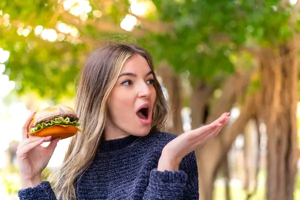 Młoda Ładna Rumuńska Kobieta Trzyma Hamburgera Świeżym Powietrzu Zaskakującym Wyrazem — Zdjęcie stockowe