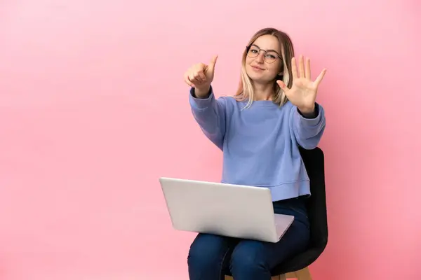 Young woman sitting on a chair with laptop over isolated pink background counting six with fingers