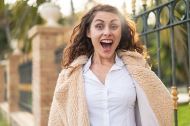 Yüzünde sürpriz bir ifade olan açık havada beyaz bir kadın.