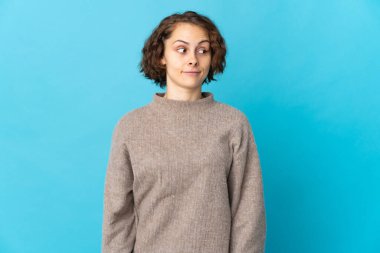 Mavi arka planda izole edilmiş genç bir İngiliz kadın şüpheli hareketler yapıyor.