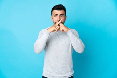 İzole edilmiş mavi arka planda beyaz bir adam sessizlik işareti gösteriyor.