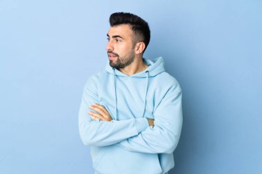 İzole edilmiş mavi arka planda beyaz bir adam yan tarafa bakıyor.