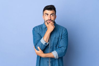 İzole edilmiş mavi arka plan üzerinde beyaz bir adam yukarı bakarken bir fikir düşünüyor.