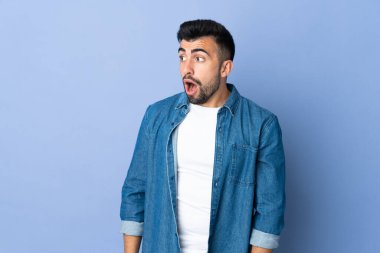 İzole edilmiş mavi arka plan üzerinde beyaz bir adam yan tarafa bakarken sürpriz jest yapıyor.