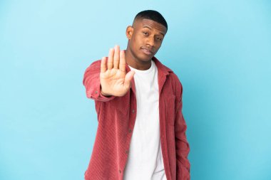 Mavi arka planda izole edilmiş genç latin adam dur hareketi yapıyor.