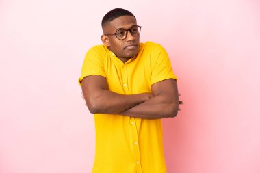 Pembe arka planda izole edilmiş genç Latin adam omuzlarını kaldırırken şüphe jestleri yapıyor.