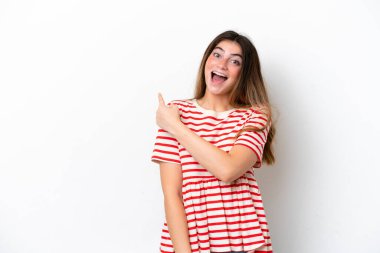 Beyaz arka planda izole edilmiş genç beyaz kadın şaşırmış ve işaret ediyor.