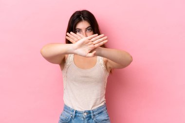 Pembe arka planda izole edilmiş genç beyaz kadın bir hareketi durdurmak için eliyle jest yapıyor.