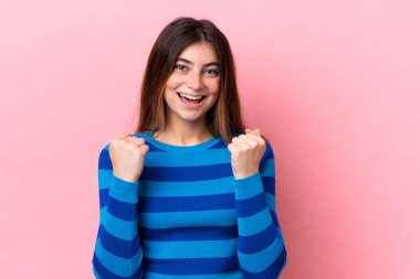 Pembe arka planda izole edilmiş genç beyaz kadın galibiyeti kutluyor.