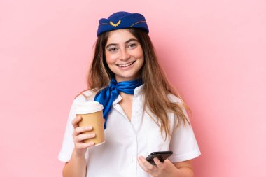 Airplane stewardess caucasian woman isolated on pink background holding coffee to take away and a mobile
