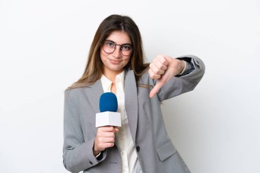 Beyaz arka planda izole edilmiş beyaz bir televizyon sunucusu olan genç beyaz kadın olumsuz bir ifadeyle baş parmağını aşağı gösteriyor.