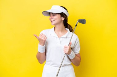 Sarı arka planda izole edilmiş golf oynayan genç beyaz kadın bir ürünü sunmak için kenarı işaret ediyor.