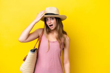 Sarı arka planda izole edilmiş plaj çantası tutan genç beyaz kadın yan tarafa bakarken sürpriz jest yapıyor.