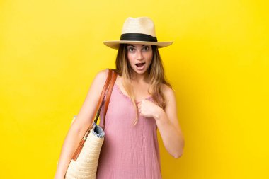 Young caucasian woman holding a beach bag isolated on yellow background with surprise facial expression
