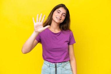 Sarı arka planda izole edilmiş genç beyaz kadın parmaklarıyla beşi sayıyor.