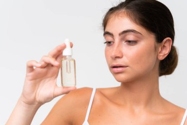 Young Pretty caucasian woman isolated on white background holding a serum. Close up portrait
