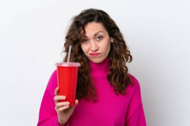 Beyaz arka planda izole edilmiş gazoz içen genç beyaz kadın üzgün bir ifadeyle