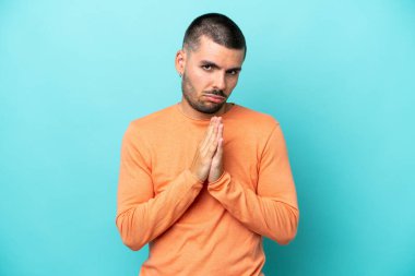 Mavi arka planda izole edilmiş genç beyaz adam avuç içlerini bir arada tutuyor. İnsan bir şey ister.