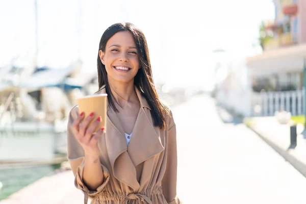 Young woman at outdoors holding a take away coffee at outdoors with happy expression