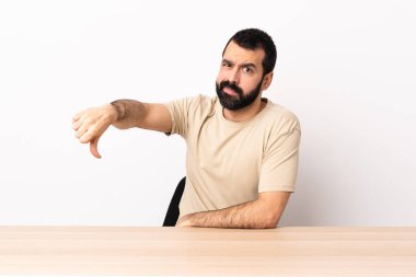 Masada sakallı beyaz bir adam, olumsuz bir ifadeyle baş parmağını aşağı gösteriyor..