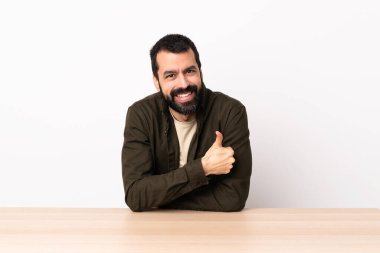 Masada sakallı, beyaz bir adam baş parmak hareketi yapıyor..