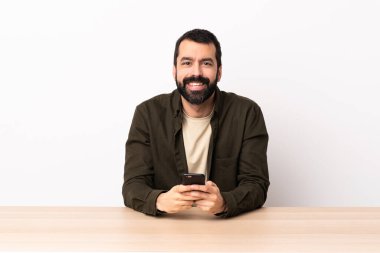 Masada sakallı beyaz bir adam cep telefonuyla mesaj yolluyor..