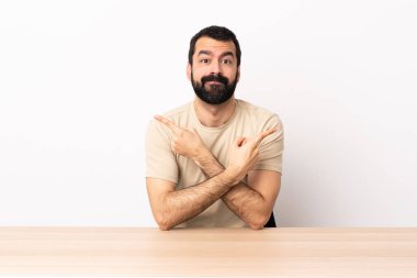 Masada sakallı, beyaz bir adam. Yan tarafı işaret ediyor. Şüpheleri var..