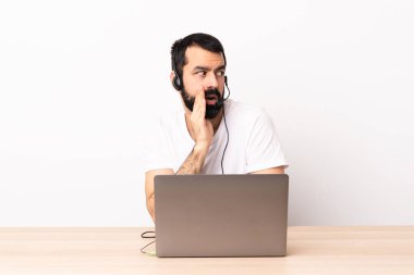 Tele pazarlamacı beyaz adam kulaklıkla çalışıyor ve laptopuyla yan tarafa bakarken sürpriz bir jest yaparak bir şeyler fısıldıyor..