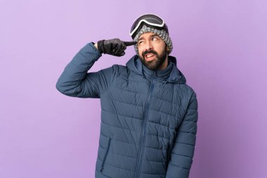 İzole edilmiş mor arka planda snowboard gözlüklü kayakçı deliliğin hareketini yapıyor. Parmağını kafaya koyuyor.