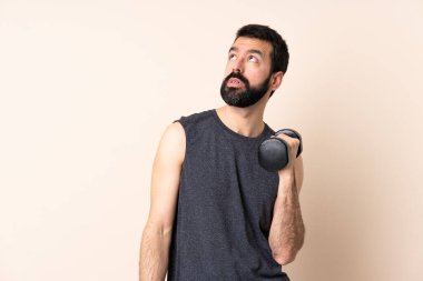 Sakallı, beyaz tenli bir sporcu izole edilmiş arka planda ağırlık kaldırıyor.