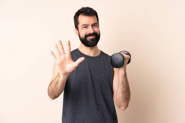 Beyaz sakallı sporcu, izole edilmiş arka planda ağırlık kaldırıyor parmaklarıyla beşi sayıyor.