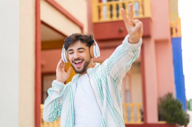 Yakışıklı bir Arap açık havada müzik dinliyor ve şarkı söylüyor.