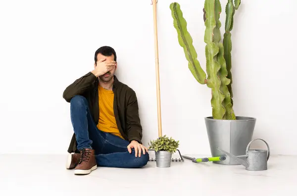 Gardener man sitting on the floor at indoors covering eyes by hands. Do not want to see something