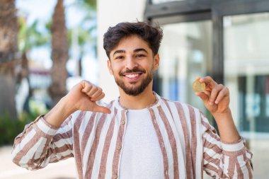 Açık havada Bitcoin tutan yakışıklı bir Arap gururlu ve kendini beğenmiş.