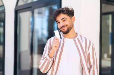 Açık havada elinde kredi kartıyla gezen yakışıklı bir Arap.
