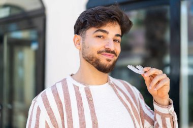 Dışarıdaki yakışıklı Arap adam görünmez diş telleri tutuyor.