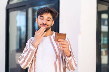 Dışarıdaki yakışıklı Arap bir cüzdan tutuyor ve ona bakıyor.